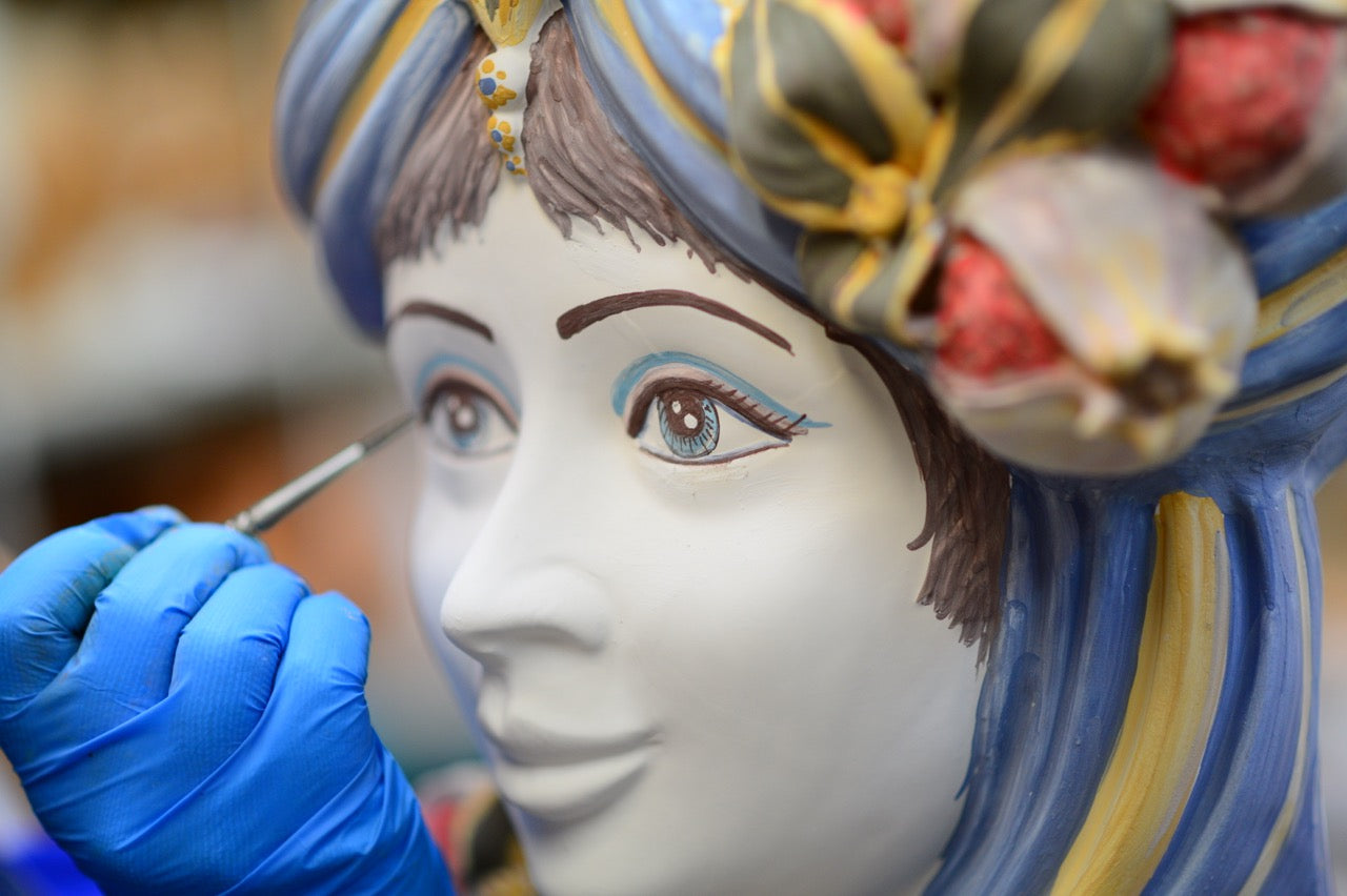 Ceramiche di Caltagirone fatti a mano: artigiano dipinge occhi su statua in ceramica con guanto blu